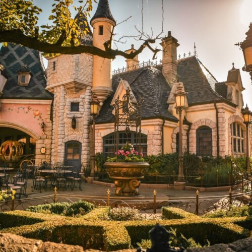 N034235 Groene struiken en boom voor het roze gebouw van Auberge de Cendrillon in Fantasyland