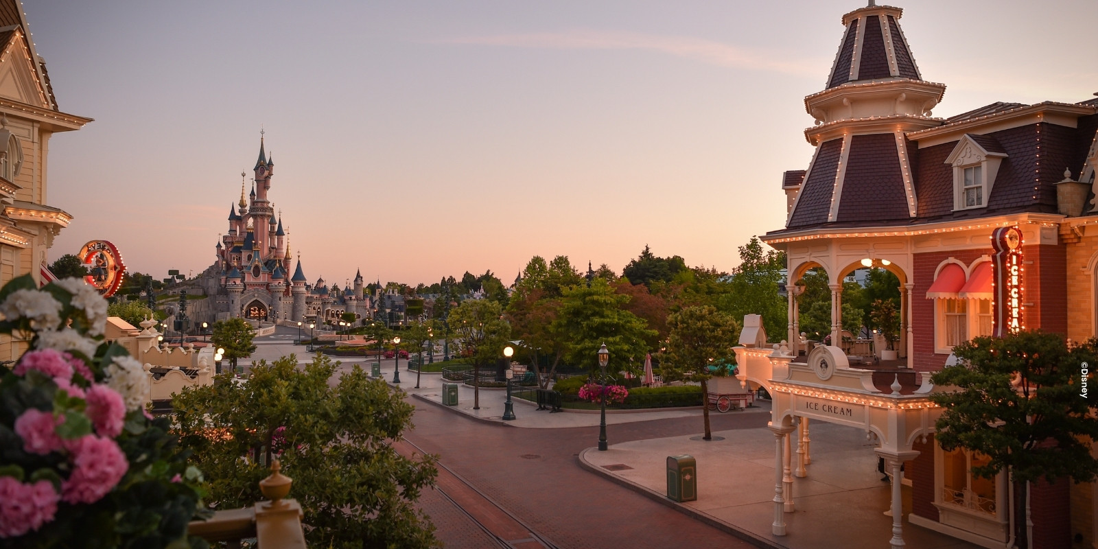 Mainstreet U.S.A.® met uitzicht op het kasteel vanaf een balkon met roze en witte bloemen in het Disneyland® Park